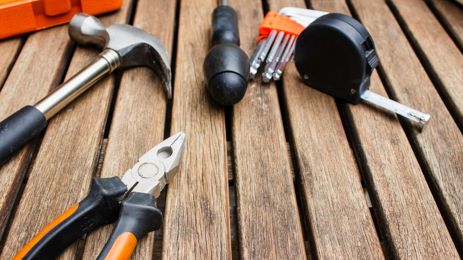 A variety of hand tools used for repairs, laying on a wooden deck floor.
