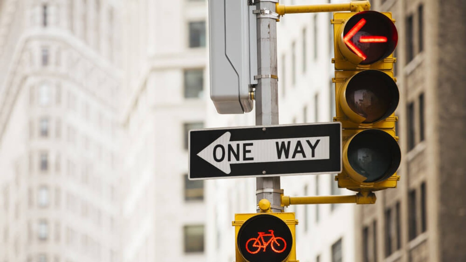 A one-way sign at a busy intersection, with a red arrow light pointing the same direction as the one-way sign.
