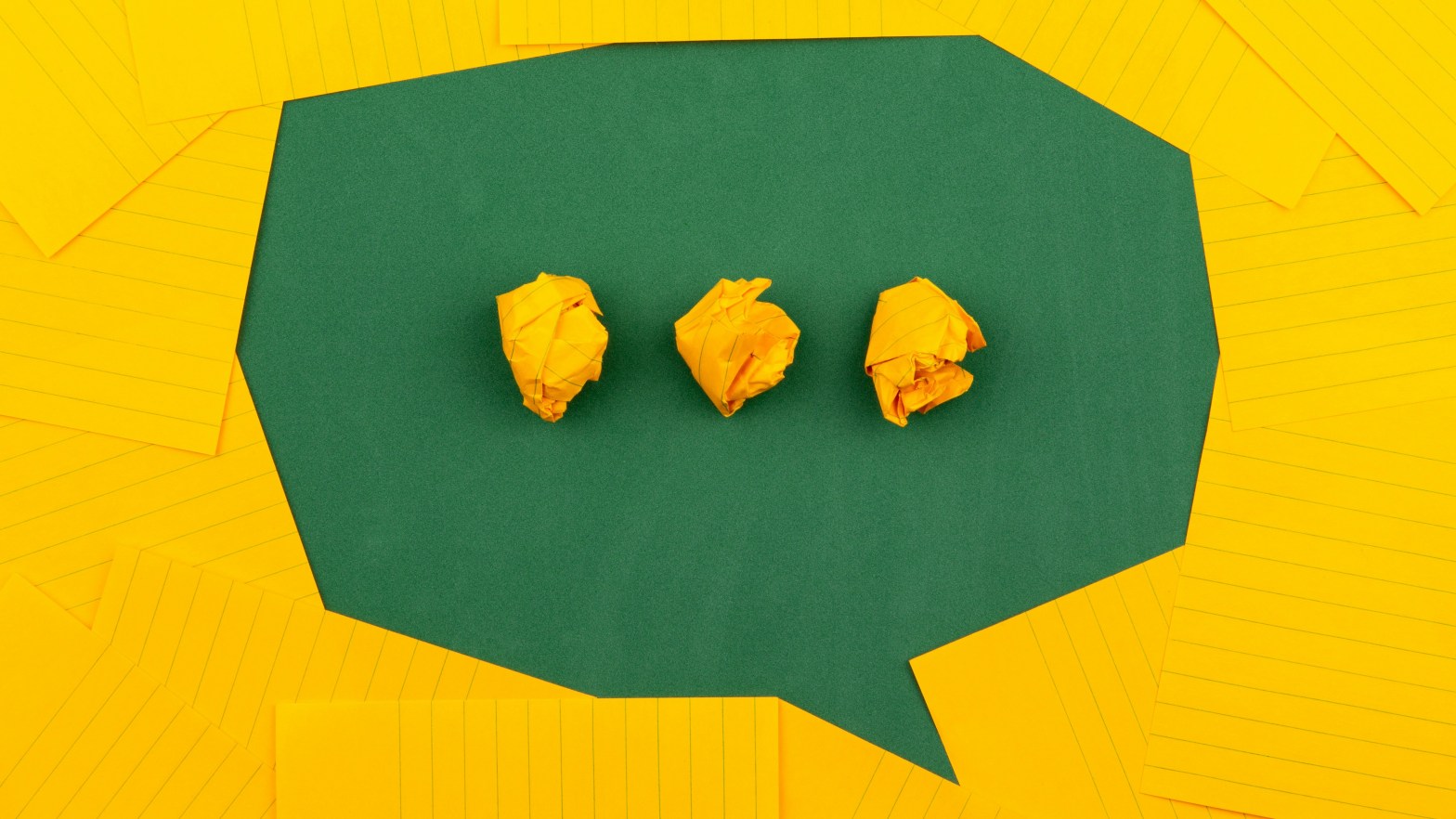 Orange sheets of paper lie on a green school board and form a chat bubble with three crumpled papers.